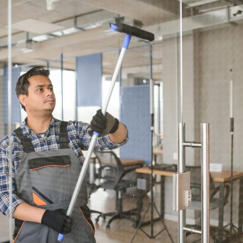 Male janitor cleaning window in office.